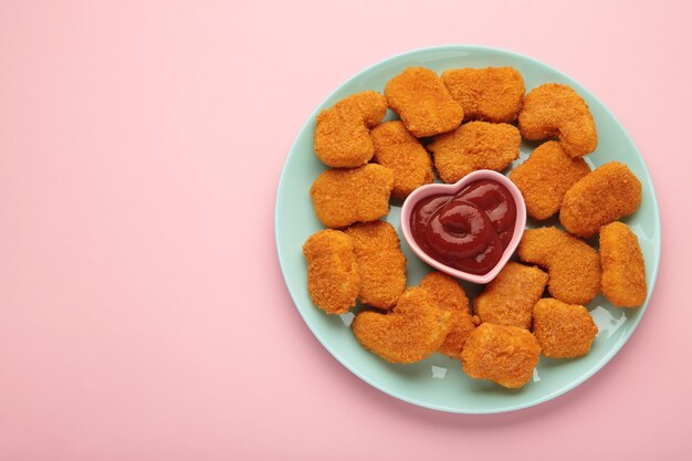 Nuggets di pollo con ketchup su piatto su sfondo rosa