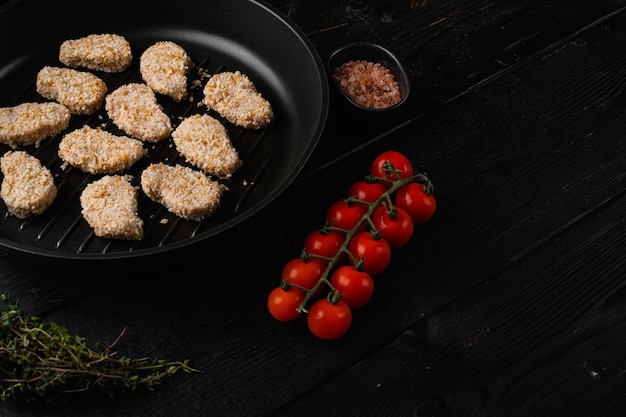 Nuggets di pollo impanati crudi fatti in casa su sfondo di tavolo in legno nero con spazio per la copia del testo