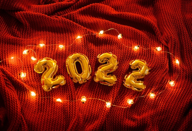 Numeri 2022 sullo sfondo di un plaid accogliente lavorato a maglia rosso e luci di Natale.