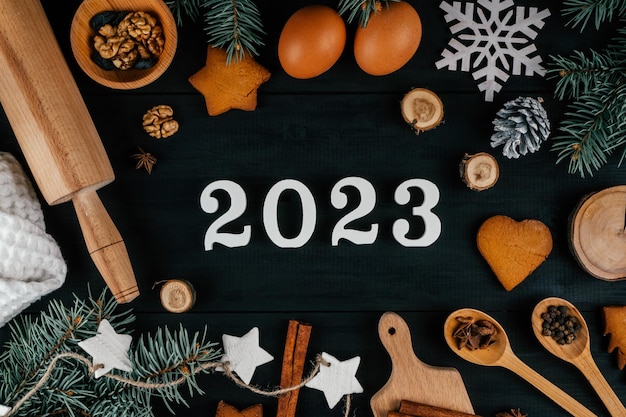 Numeri bianchi 2023 sdraiati su un tavolo nero con accessori e ingredienti per la cottura dell'albero di Natale Capodanno 23 Vista dall'alto