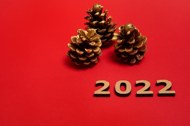 Numeri in legno sdraiati su sfondo rosso accanto alle pigne di Natale dipinte in colore dorato, con spazio per la copia per la pubblicità di Capodanno. Celebrazione, evento, concetto di vacanze