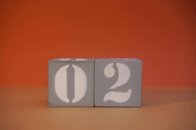 Numero 02 su cubi grigi di legno primo piano Concetto di data e ora Concetto matematico Copia spazio per testo o evento Numeri bianchi 2 su blocchi di costruzione sfondo arancione Messa a fuoco selettiva
