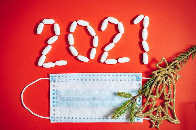 Numero 2021 composto da pillole e mascherina medica protettiva su fondo rosso.
