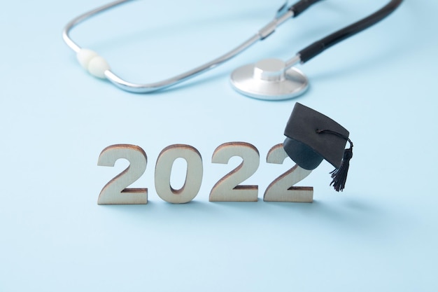 Numero 2022 che indossa un berretto laureato con stetoscopio medico su sfondo blu. L'educazione medica nel concetto 2022