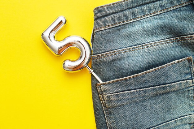 Numero 5 che spunta dalla tasca posteriore dei jeans blu su sfondo giallo