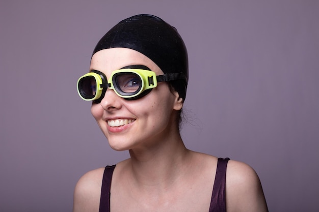 nuotatore donna sorridente in una cuffia occhiali e uno sfondo grigio costume da bagno