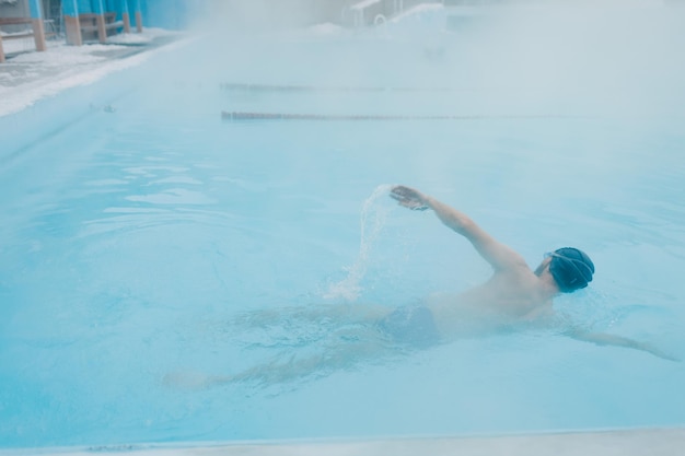 Nuoto di allenamento maschile in forma nuotata in una piscina invernale aperta con nebbia Concetto di spa geotermica all'aperto