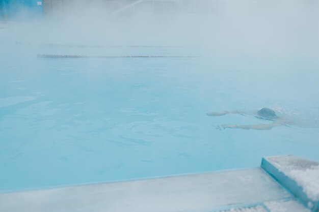 Nuoto di allenamento maschile in forma nuotata in una piscina invernale aperta con nebbia Concetto di spa geotermica all'aperto