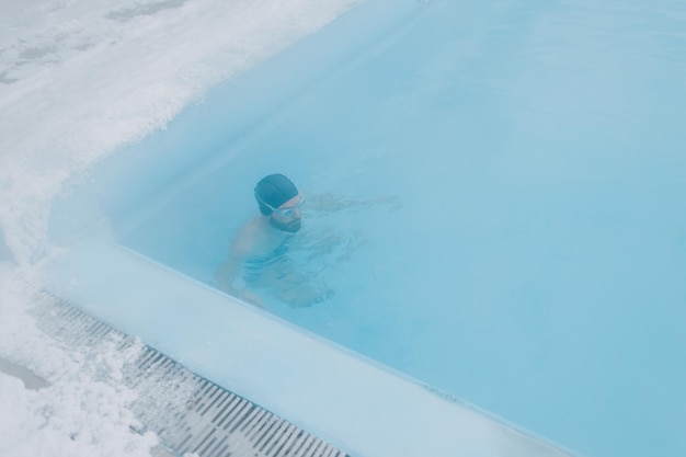 Nuoto di allenamento maschile in forma nuotata in una piscina invernale aperta con nebbia Concetto di spa geotermica all'aperto