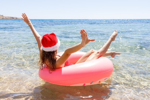 Nuoto pazzo con ciambella gonfiabile e cappello di Natale sulla spiaggia in una giornata di sole estivo