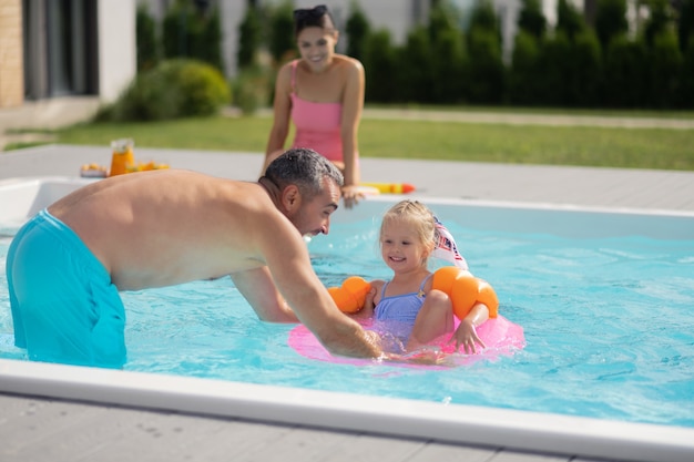 Nuoto vicino a papà. Allegra bella figlia adorabile che si sente felice mentre nuota vicino a papà da