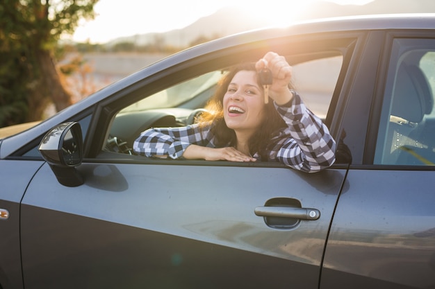 Nuova automobile, acquisto e concetto del driver - Giovane donna che mostra la chiave in una macchina.