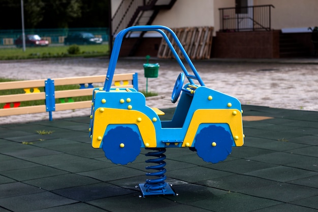 Nuova grande automobile blu e gialla variopinta luminosa di plastica moderna del giocattolo sulla molla del campo da giuoco della scuola materna con la pavimentazione di gomma morbida il giorno di estate soleggiato luminoso. Luogo perfetto per attività per bambini all'aperto.