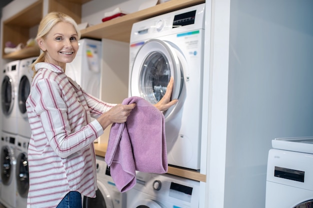 Nuova lavatrice. Donna bionda in camicia a righe in piedi vicino alla lavatrice