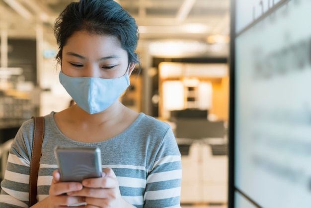 Nuova normalità dopo l'epidemia di covid19 intelligente asiatico femminile antiusura maschera di protezione uso manuale smartphone comunicazione nel grande magazzino nuovo stile di vita astratto sfocatura dello sfondo