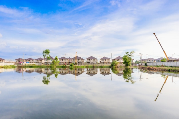 Nuova riflessione della costruzione della casa con acqua nel lago al cantiere della tenuta residenziale con le nuvole ed il cielo blu