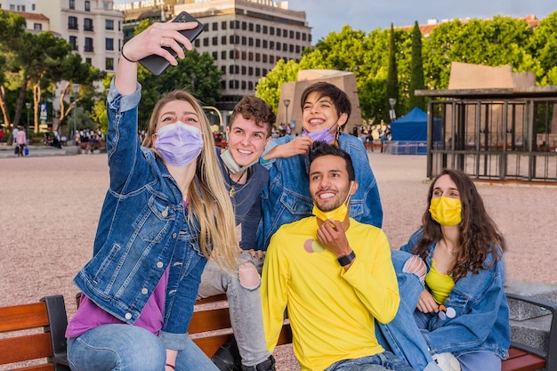 Nuova vita normale del virus corona con un gruppo multirazziale di giovani studenti che si fa un selfie con la maschera facciale