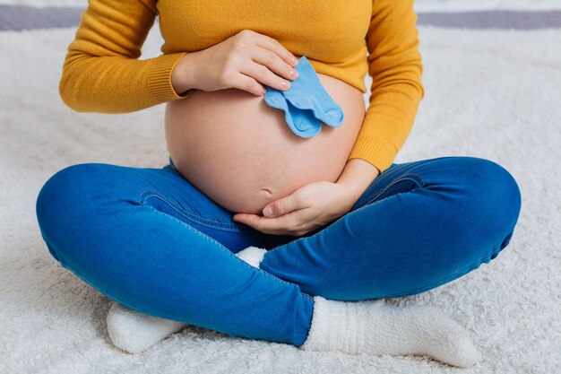 Nuova vita sotto il cuore. Giovane futura mamma che attraversa le gambe, abbracciando il pancione mentre è a casa