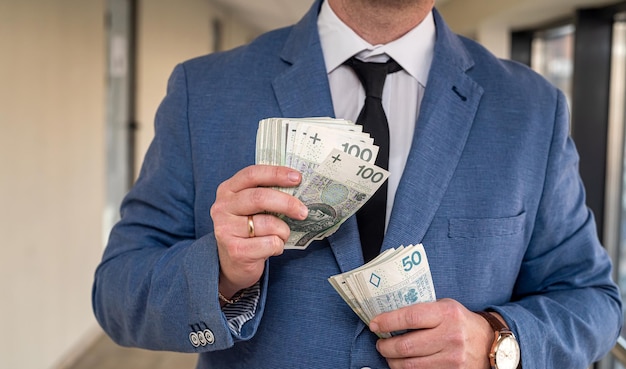 Nuove banconote in zloty polacche nelle mani di un uomo d'affari in giacca e cravatta