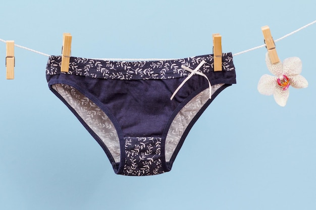 Nuove mutandine di cotone nero su stendibiancheria con mollette e fiori di orchidea su sfondo blu. Intimo donna.