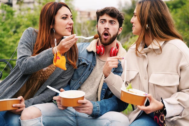 Nuovi amici normali che si riuniscono con persone felici che scherzano mangiando cibo da asporto da ciotole prive di plastica che indossano una maschera facciale al polso. Concetto di persone che si divertono, reunion post blocco covid