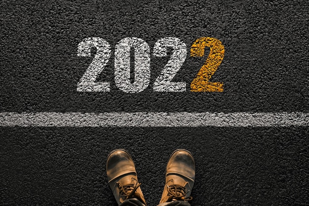 Nuovo anno 2022, concetto. L'uomo fa il primo passo nel nuovo anno. Scarpe da uomo sull'asfalto vicino alla linea con i numeri 2022, idea creativa.