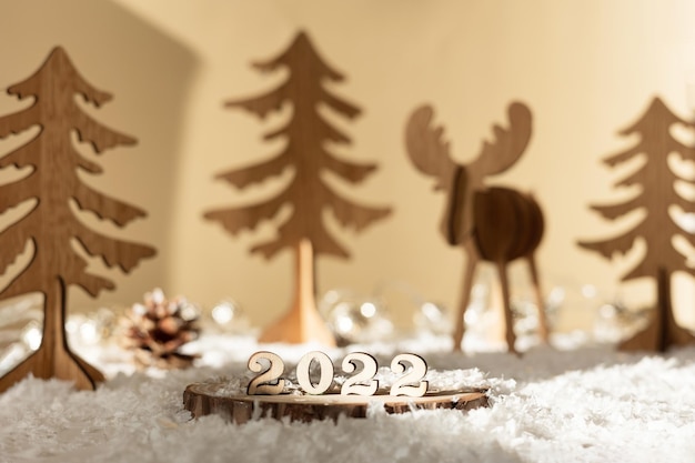 Nuovo anno 2022. Numeri 2022 su supporto in legno su sfondo sfocato pastello beige con cervi decorativi, abeti, neve e luci. Biglietto di auguri di Natale.