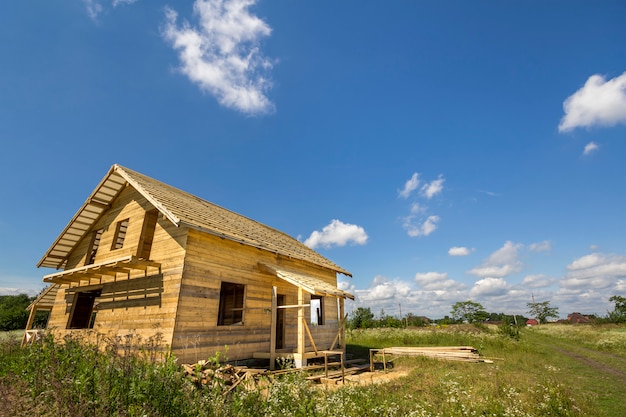 Nuovo cottage tradizionale ecologico di legno dei materiali naturali del legname con il tetto ripido in costruzione in vicinanza verde sullo spazio della copia del cielo blu. Concetto di costruzione professionale.