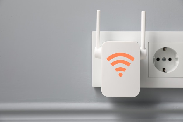 Nuovo ripetitore moderno con simbolo WiFi inserito nella presa sullo spazio della parete grigio chiaro per il testo