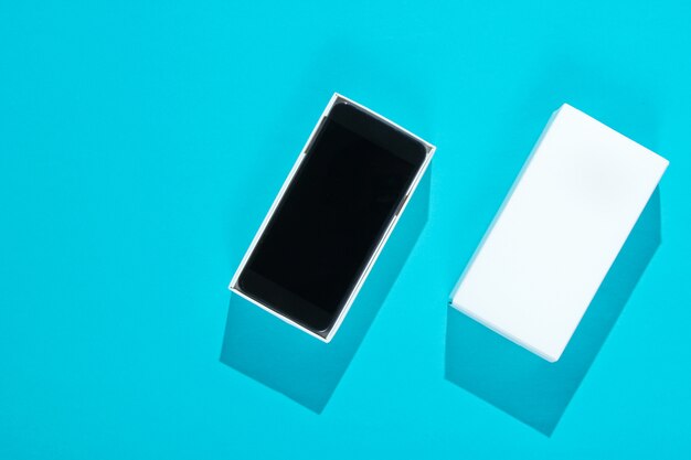 Nuovo smartphone in scatola aperta sul tavolo di carta blu. Vista dall'alto, minimalismo