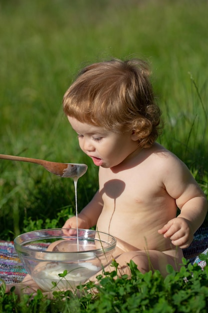 Nutrire il bambino con un cucchiaio all'aperto su erba verde razione estiva assistenza all'infanzia buongiorno in fattoria