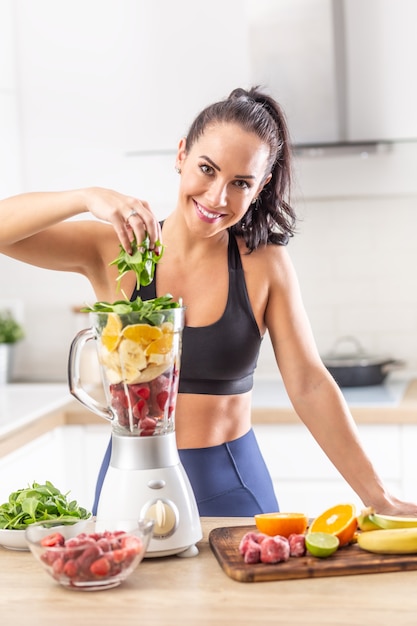 Nutrizione post-allenamento per una donna in abiti da fitness sotto forma di bacche rosse, arance e spinaci in un frullatore.
