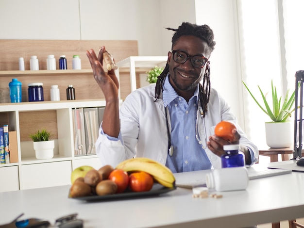 Nutrizionista afroamericano guardando la fotocamera e mostrando frutti sani nella consultazione