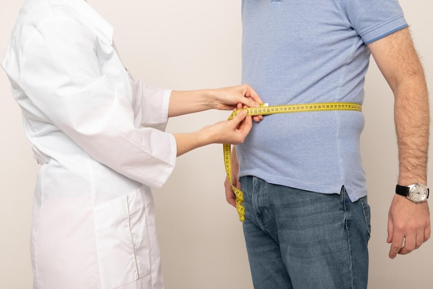 Nutrizionista che misura la vita di un uomo in sovrappeso con un nastro adesivo in clinica