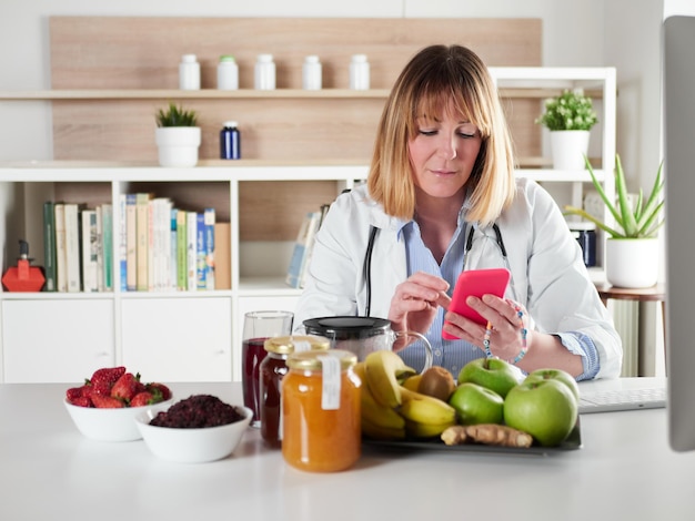 Nutrizionista femminile distratto che chiacchiera con lo smartphone nello studio dell'ufficio