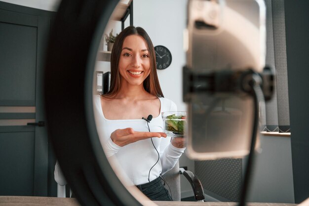 Nutrizionista sta mostrando insalata sulla fotocamera Giovane bella donna in abiti bianchi è in ufficio