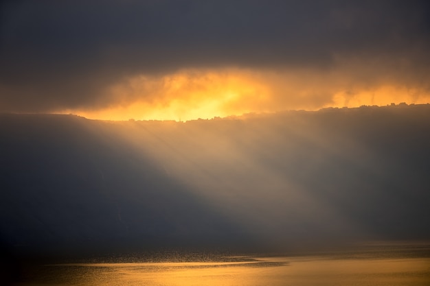 Nuvole pesanti sulla costa rocciosa. I raggi del sole irrompono appena, illuminano le piccole case e la superficie dell'acqua