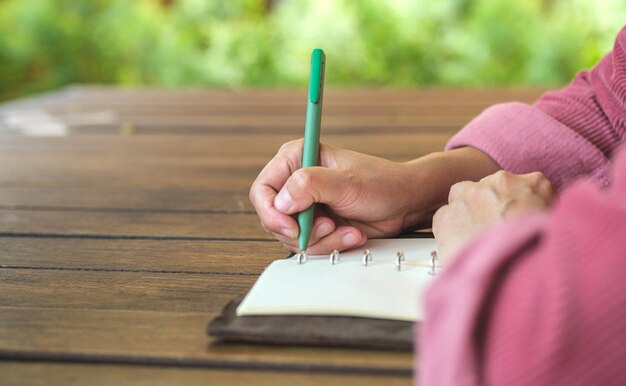 Obiettivo di scrittura della donna sul taccuino allo spazio all'aperto della caffetteria