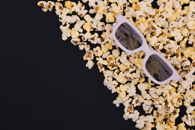 Occhiali 3d e popcorn sono isolati su uno sfondo nero. Disteso. Copyspace. Concetto di cinema