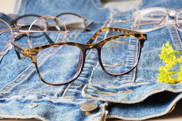 Occhiali alla moda su una giacca di jeans, una vecchia giacca fatta di blue jeans e occhiali multipli, montature per occhiali alla moda