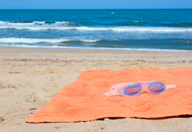 Occhiali da mare blu su un asciugamano arancione in riva al mare