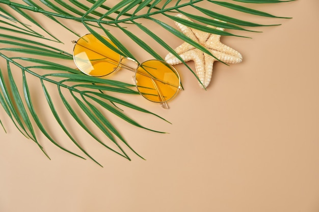 Occhiali da sole gialli e foglie di palma vista dall'alto sulla superficie beige