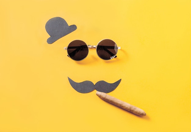 Occhiali da sole hipster e baffi divertenti con cappello e sigaro su giallo