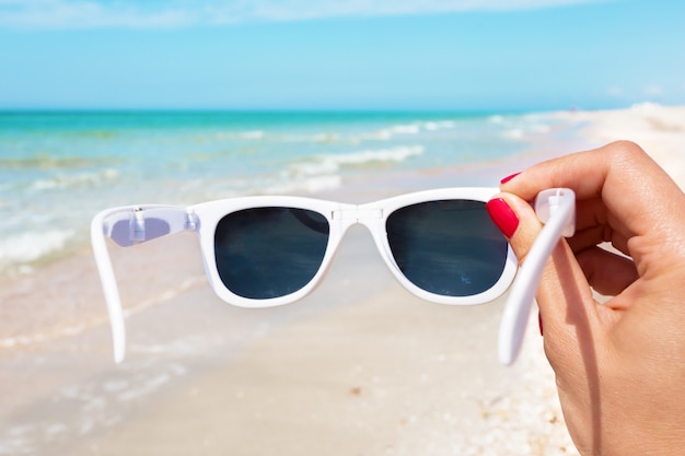 Occhiali da sole in mano sullo sfondo della spiaggia