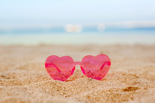 Occhiali da sole rosa su una spiaggia sabbiosa con un fondo blu del mare, luna di miele, vacanza, spazio della copia