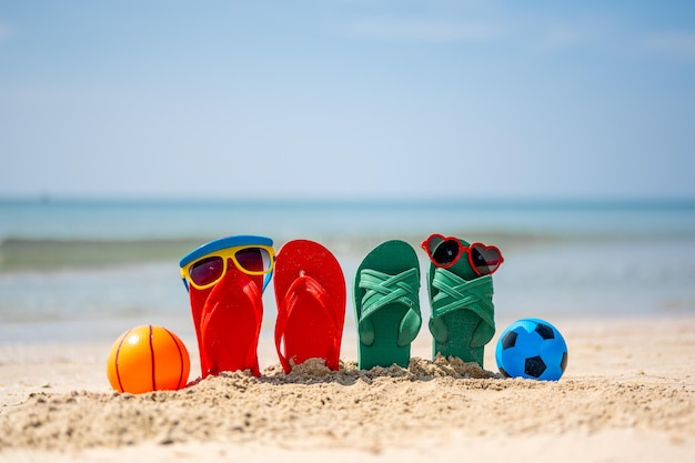 Occhiali da sole rossi e gialli infradito rossi e verdi sulla sabbiacalcio giocattolo Viaggiare in mare Vacanze al mareSpiaggia sabbiosa tropicale viaggi estivi vacanze e vacanze estive concetti