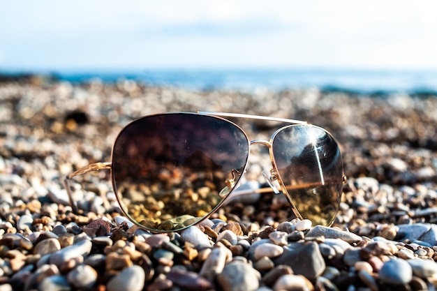 Occhiali da sole sdraiati su una spiaggia di ciottoli con il sole che splende su di loro.