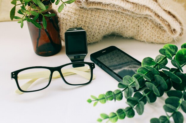 occhiali da telefono e orologi elettronici si trovano accanto a una pianta verde