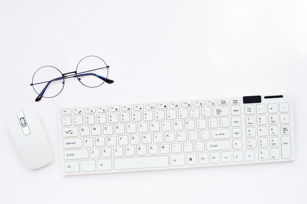 Occhiali da vista con tastiera del computer bianco e mouse del computer su sfondo bianco