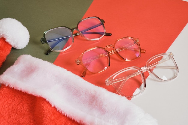 Occhiali da vista multipli e cappello da Babbo Natale su sfondo rosso e verde, vendita di negozi di ottica prima dello spazio della copia di natale